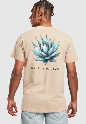 Beige bomulds T-shirt med et stort, detaljeret grafik af en blå-grøn agaveplante på ryggen med teksten "SALT, SIP, LIME" nedenunder.