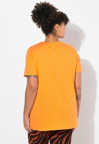 Kortærmet orange t-shirt lavet af glat bomuld, med rund halsudskæring og afslappet pasform, parret med mønstrede orange og sorte leggings.