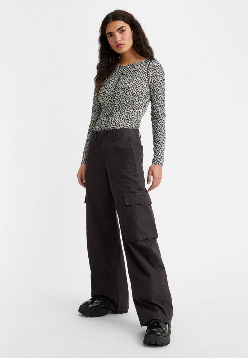 Haut à manches longues avec un motif floral noir et blanc, associé à un pantalon cargo noir ample doté de poches latérales et d'une coupe droite.
