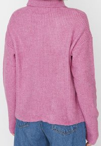 Rückansicht einer Person, die einen rosa gestrickten Pullover mit langen Ärmeln und blaue Jeans trägt.