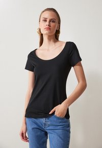Svart t-skjorte med korte ermer og rund hals, laget av myk stoff. Stylet med avslappede blå jeans, som viser en figursydd silhuett.