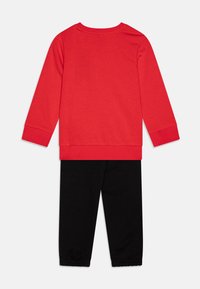 Top rojo de manga larga con cuello redondo y pantalones negros ajustados. El top presenta puños acanalados y los pantalones tienen elástico en los tobillos.