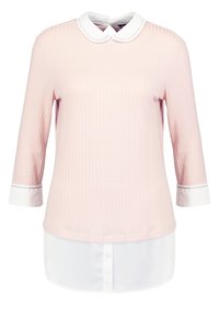Haut rose côtelé avec manches trois-quarts, col et poignets blancs, bas blanc superposé avec détails de boutons.