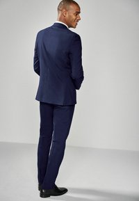 Navy suit with a fitted design, smooth texture, and delicate lapels. Black shoes complement the tailored look. Clean, minimalist background.