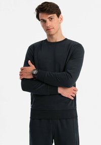 Svart crew neck sweatshirt i texturerad tyg, med ribbade muddar och nederkant, bärs över matchande svarta byxor.