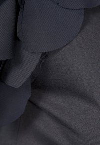 Tessuto blu navy dalle superfici lisce con motivi floreali sovrapposti. Il corpo principale appare leggermente strutturato, creando un contrasto visivo.