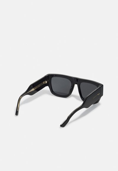 Occhiali da sole neri a forma quadrata con lenti scure, montatura in plastica audace, dettagli in tono oro sulla parte delle tempie e design elegante.