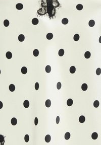 Tissu blanc à pois noirs régulièrement espacés et une bande de dentelle noire en haut.