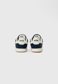 Navy blue sneakers with textile and leather upper, cream accents, and brown rubber sole. Positioned from the back, highlighting heel detail.