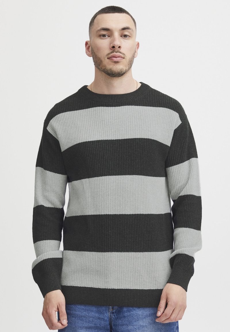 Pulover tricotat cu dungi orizontale îndrăznețe negre și gri, textură ribbed, mâneci lungi și guler rotund.