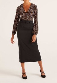 Svart blyertskjol kombinerad med en långärmad omlottopp med ett färgglatt lövmönster. Toppen har en djup V-ringning och luftiga ärmar.