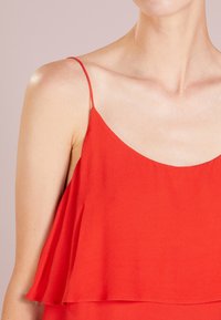 Haut rouge sans manches avec un design ample et aérien. Confectionné en tissu doux, avec un décolleté plongeant et de fines bretelles. Texture lisse.