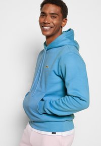 Lichtblauwe hoodie gemaakt van zachte stof, met een kangoeroe-pocket, verstelbare trekkoord en geborduurd logo op de borst.