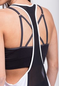 Débardeur sportif noir avec des accents blancs, doté d'un dos plongeant et de bretelles croisées. Le matériau est extensible et respirant.