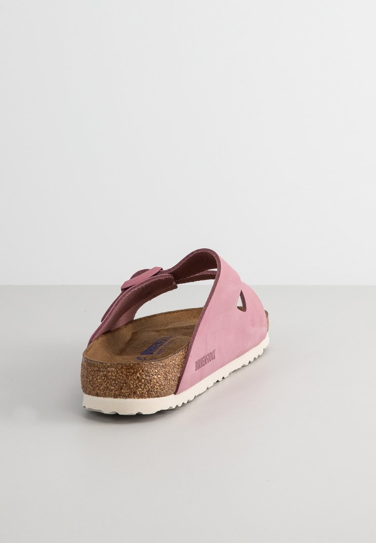 Rosa Birkenstock-Sandale mit weichem Obermaterial, Korkfußbett und weißer Gummisohle mit einer Aussparung im Design der Riemen.