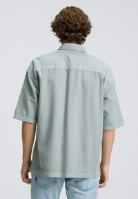 Korte mouwen shirt van lichtgroene stof met een zachte textuur, voorzien van een klassieke kraag en een rechte snit, gedragen met lichtblauwe jeans.