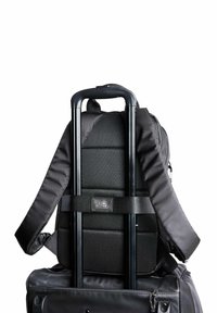 Czarny plecak przymocowany do uchwytu czarnej walizki na kółkach, z wyściełanymi paskami i widoczną metką "camel active".