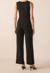 Mono negro con un cuerpo entallado y pantalones de pierna ancha, que presenta un discreto cierre en la parte posterior y una tela suave y texturizada.