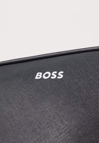 Černý texturovaný materiál s výrazným bílým logem "BOSS" a hladkým lemováním, které zvýrazňuje design.