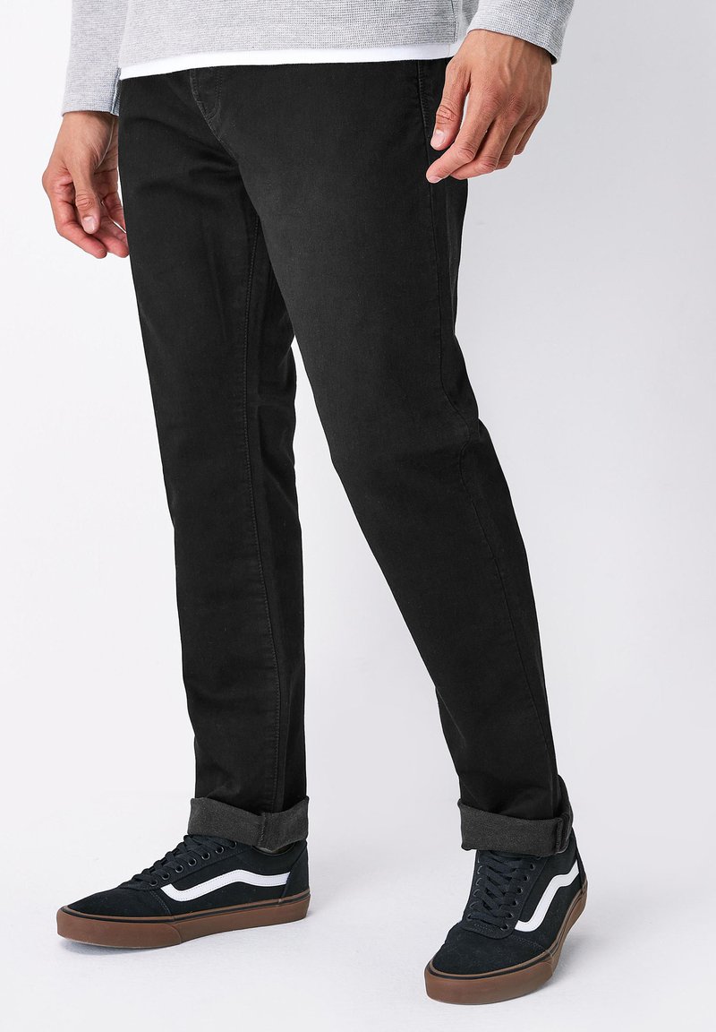 Jeans de mezclilla negra con un corte recto, que presentan detalles de costura sutiles. Llevados con zapatillas altas negras con acentos blancos y puños doblados.