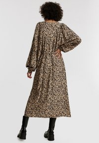 Vestido largo y holgado en beige con un estampado de animal en negro, que presenta mangas abullonadas y una cintura ajustada. Tejido suave con un diseño fluido.