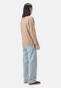 Langes Shirt mit entspanntem Sitz, kombiniert mit hellblauen weiten Jeans und dunklen Slip-On-Schuhen. Einfaches Design, weiche Textur.