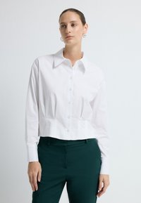Witte, cropped button-up shirt met lange mouwen, klassieke kraag en een soepele textuur, gecombineerd met donkergroene, op maat gemaakte broek.