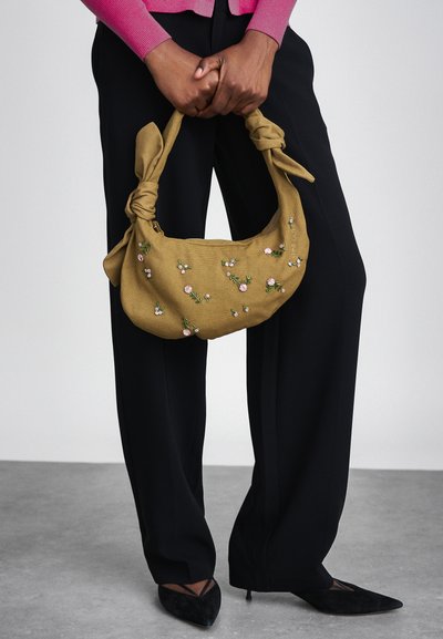 Olivaroheline kangaskott lillekirjao ja sõlmehandlesidega. Sile tekstuur, keskmise suurusega, lukuga sulgemine turvalisuse tagamiseks.