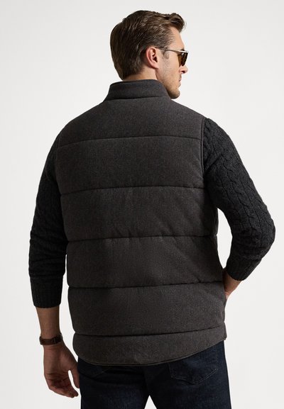 Vestă matlasată cu mâneci tricotate în model torsadă, culoare cărbune închis, textură matlasată și guler înalt. Purătată peste o cămașă neagră, vedere din spate.