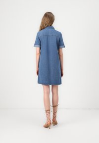 Denim skjortekjole i middels blå, med kragehals og rullede korte ermer, med en rett silhuett og knelengde.