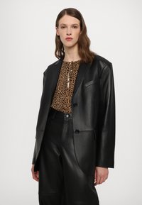 Čierny kožený blazer so štruktúrovaným dizajnom, so zapínaním na dva gombíky, spárovaný s hnedou blúzkou s leopardím vzorom a čiernymi koženými nohavicami.