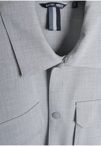 Lichtgrijs button-up shirt met een spread collar, twee borstzakken en een gestructureerde stof met subtiele lijnen. Label zichtbaar bij de hals.