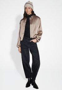 Satin bomber jacket in taupe, ribbed black top, wide-leg black jeans, and black heeled boots, with a light-colored knitted beanie.