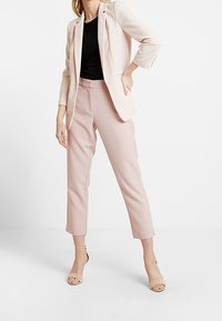 Jasnoróżowa marynarka i dopasowane zwężane spodnie, zestawione z czarnym topem. Dopełnieniem stroju są cieliste sandałki na paski. Gładka tkanina i dopasowany krój.