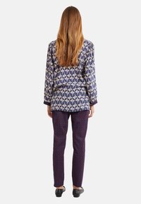 Blusa a maniche lunghe con motivo blu e crema, caratterizzata da un design geometrico, abbinata a pantaloni navy slim-fit con pois rossi e scarpe nere.
