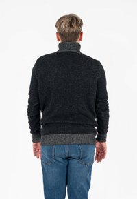 Ciemnoszary sweter z wysokim kołnierzem, teksturowana tkanina, oraz ściągacze i dół w prążki. Połączony z niebieskimi dżinsami, widok z tyłu.