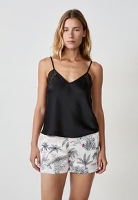 Camisole en satin noir avec des fines bretelles et des accents en mesh, associé à un short blanc avec un motif de plantes tropicales en noir et des détails colorés.