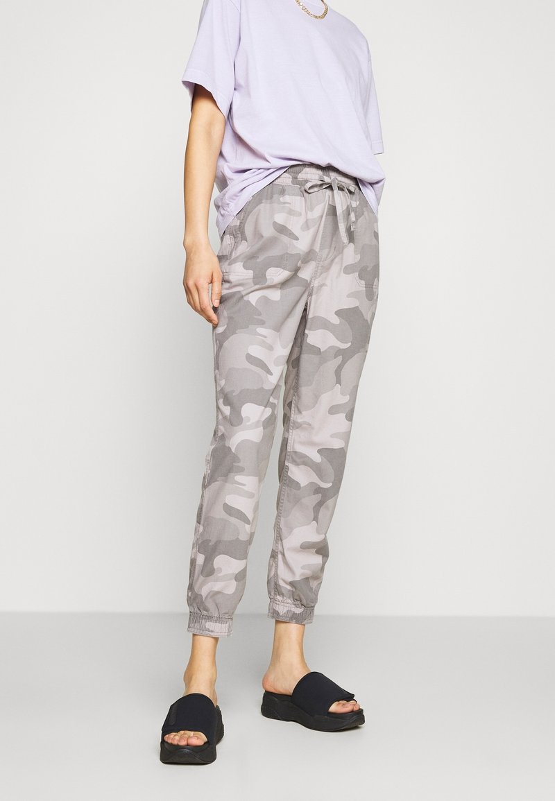 Pantalons de camouflage gris avec taille élastique et cordon de serrage. Associés à un t-shirt lilas et des sandales noires à enfiler.