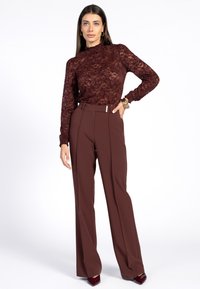 Bordeaux kanten top met hoge hals en lange mouwen, gecombineerd met hoog getailleerde, verfijnde bruine broek met een elegante riemdetail.