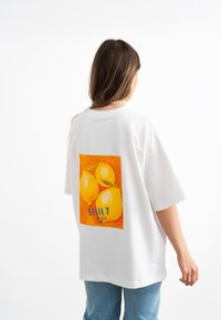 T-shirt bianca oversize con un vivace grafico giallo e arancione di tre limoni con la scritta "Sicilia Italia" sotto. Materiale in cotone.