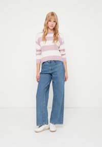 Pull en maille rayé rose clair et blanc avec des manches longues, associé à un jean en denim bleu à jambes larges et des baskets blanches.