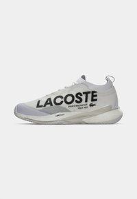 Fehér és szürke Lacoste sneaker zokni-szerű gallérral, nagy fekete logó felirattal és párnázott talppal, amelyen az "LSRFOAM" felirat található, fehér háttérrel.