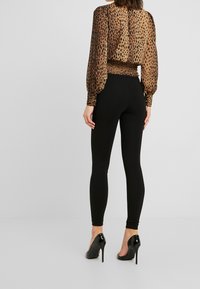 Brun leopardmönstrad blus med samlad midja och långa ärmar. Svarta, tajta leggings. Skor i svart med blank yta och spetsig tå.