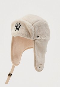 Chapeau trapper en polaire beige avec rabats d'oreilles, logo noir brodé à l'avant et sangle ajustable suspendue sous un rabat.