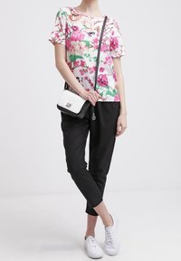 Biała bluzka z krótkim rękawem w kwiatowy wzór, zestawiona z czarnymi, zwężającymi się spodniami i białymi sneakersami. Całość uzupełnia mała czarno-biała torebka na ramię.