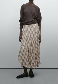 Braunes Langarmoberteil, kariert plissierter Rock in Creme-, Beige- und sanften Brauntönen. Paar schwarze Slip-On-Schuhe mit weicher Textur.