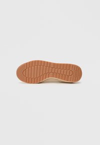 Suola in gomma beige con un motivo testurizzato e scanalature. Forma leggermente curva progettata per il comfort. Bordo rinforzato per una maggiore durata.