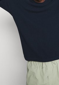 Suéter texturizado azul marino con cuello redondo, diseño recortado y puños acanalados, combinado con pantalones ligeros de color claro.