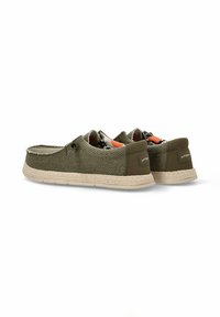 Zapatillas de lienzo verde oliva con textura tejida, suela de goma beige y forro con patrón. Presentan bordes cosidos y detalle de logo en la parte trasera.
