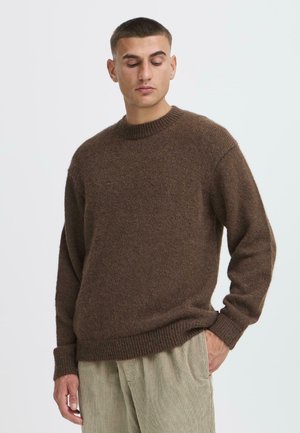 Brązowy sweter dzianinowy z okrągłym dekoltem i ściągaczami. Miękka tekstura, luźny krój, zestawiony z jasnymi spodniami z korduory.